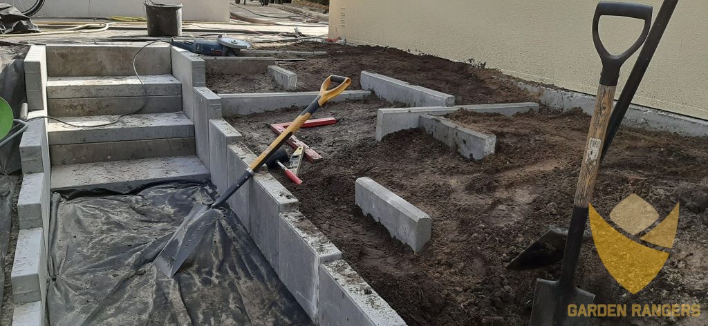 Geometryczny, ale nieregularny układ płyt betonowych stanowi o modernistycznym charakterze tej powstającej konstrukcji rabaty, schodów i murów oporowych.